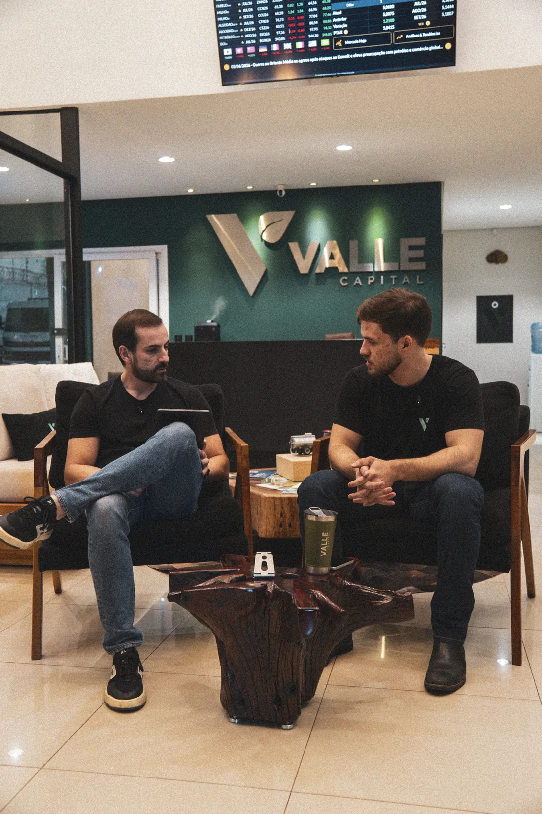Sócios da Valle conversando na recepção da Valle Capital, em frente ao logotipo